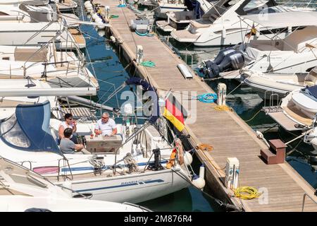 At the Club Nautico of Porto Cristo, Mallorca three friends enjoy the sunny day on a sailboat. Stock Photo