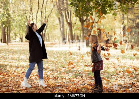 Playful, pleased, funny, glad, carefree mother and daughter playing with leaves, throw like rain in golden autumn forest Stock Photo