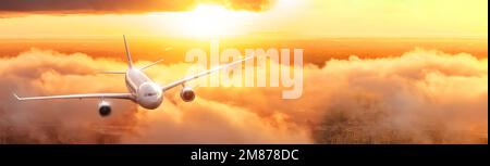 Flying airplane commercial civil airliner over the clouds during sunset dawn realistic brilliant reflected light backlit, wide banner view Stock Photo
