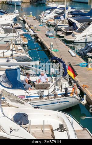 At the Club Nautico of Porto Cristo, Mallorca three friends enjoy the sunny day on a sailboat. Stock Photo