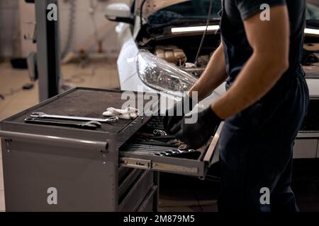 cropped Mechanic in car workshop taking working tools from shelf. unrecognizable guy in gloves and uniform is going to repair car automobile. in auto Stock Photo