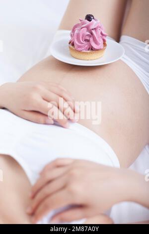 Pregnant women lie on your back in bed holding a cake Stock Photo