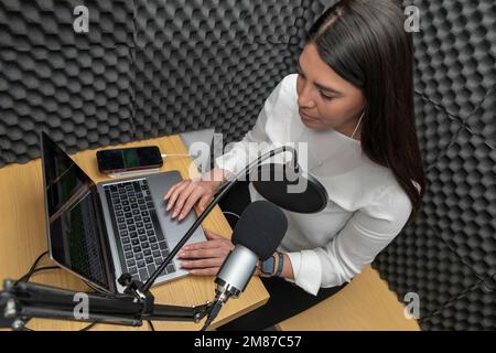 top view of a woman recording a podcast in an audio booth. Stock Photo