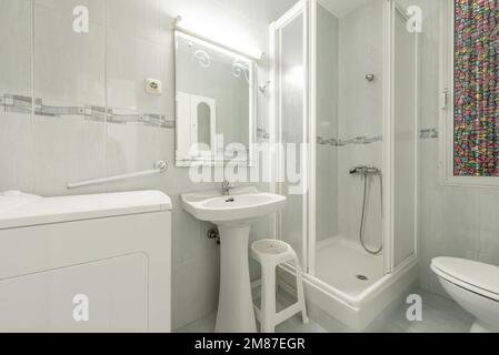 White-toned bathroom with walk-in shower, mirror, and top-loading washing machine Stock Photo