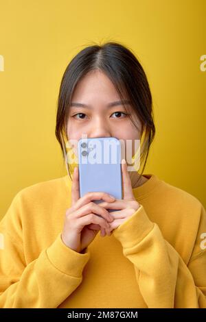 Close-up portrait of shocked chinese woman holding smartphone in hands reading message, stand looking at camera with big eyes, think what to say, surp Stock Photo