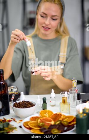 fragrance bottles used for blending scent for making perfume by perfumer in cozy modern laboratory. attractive caucasian female in uniform apron sit a Stock Photo