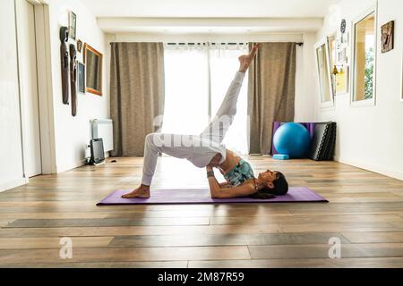 Side view of a woman practicing yoga, doing One Legged Bridge Pose (Eka Pada Setu Bandha Sarvangasana). Stock Photo