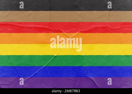Pride rainbow flag with black and brown stripes painted on cracked textured wall. Outdoor Grunge texture background Stock Photo
