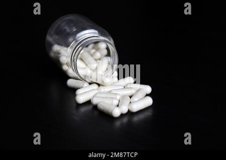 White pills on a black wooden table, medication in capsules scattered from the bottle. Background for pharmacy, antibiotics, vitamins Stock Photo
