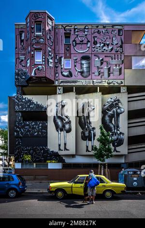 Senior white man entering a retro yellow Mercedes in front of a brutalist building with interesting graffities in Berlin Stock Photo