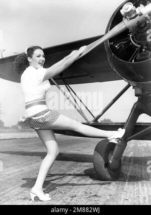 LINDA DARNELL circa 1940 leggy pose by plane Stock Photo