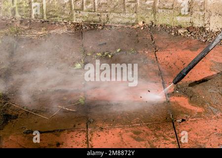 A power pressure washer using a pressurised water stream to clean a dirty stained patio Stock Photo
