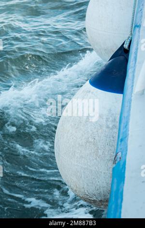 A white and blue inflatable Polyform A-Series buoy as fender on moving boat from above Stock Photo