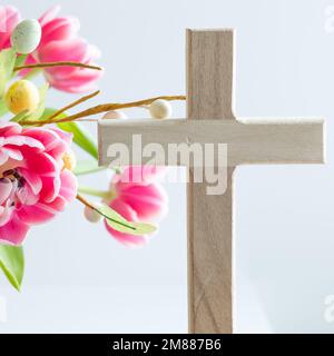 Small wood Christian cross with a bouquet of fresh pink variegated tulips and easter eggs on a white background with copy space Stock Photo