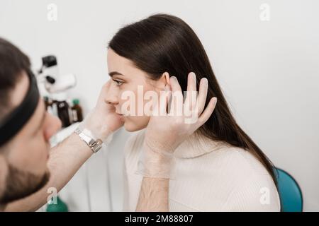 Otoplasty ear surgery. Surgeon doctor examines girl ears before otoplasty cosmetic surgery. Otoplasty surgical reshaping of pinna and ear Stock Photo