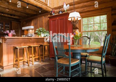 Round wooden antique dining table with high back chairs and kitchen bar with bar stools inside handcrafted Scandinavian spruce log home. Stock Photo