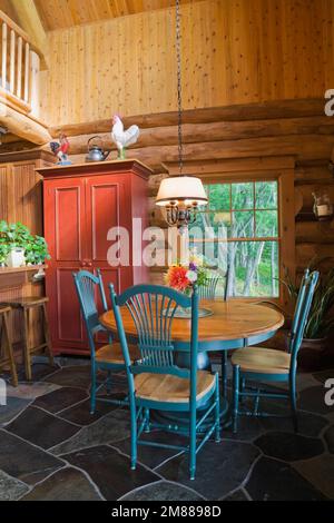 Round wooden antique dining table with high back chairs and kitchen bar with barstools inside handcrafted Scandinavian spruce log home. Stock Photo