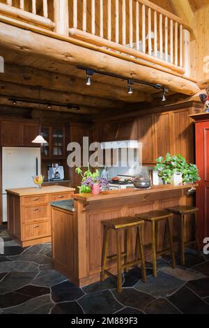 Kitchen bar with barstools in kitchen with slate tile floor inside handcrafted Scandinavian spruce log home. Stock Photo