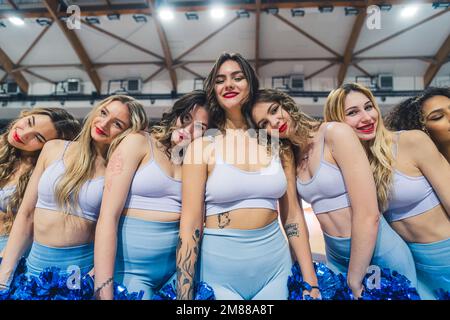 Group of cheerleaders is captured in a playful pose, resting their heads on fellow's shoulders as they smile for the camera. Cheerleaders are dressed in blue uniforms and each holds a pair of pom-poms. Stock Photo