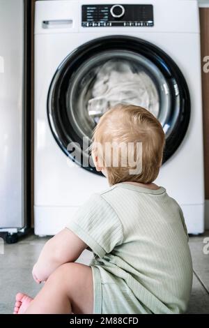 Child with washing machine. Small child looks at a working washing machine in a home laundry. High quality photo Stock Photo