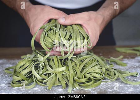 Fresh pasta. Homemade Italian raw pasta fettuccine with spinach in the hands of the chef on the background of the kitchen. High quality photo Stock Photo