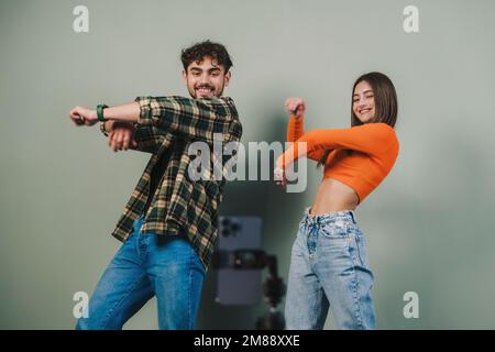 Dancing two young woman and man bloggers recording video in studio isolated over gray background. People lifestyle portrait. Stock Photo