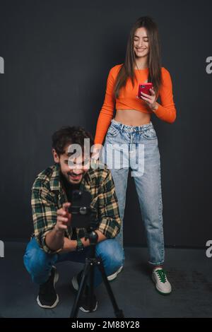 Stylish two teen bloggers shooting trendy dance for social media isolated over black background. People, music, fun, show and entertainment concept. Stock Photo