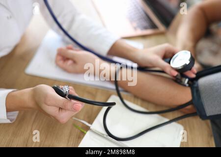 Close up of doctor using sphygmomanometer with stethoscope checks blood pressure of patient in hospital. Stock Photo