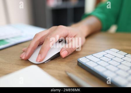 Close-up of business woman's hand holding computer mouse on office desk with keyboard and documents. Stock Photo