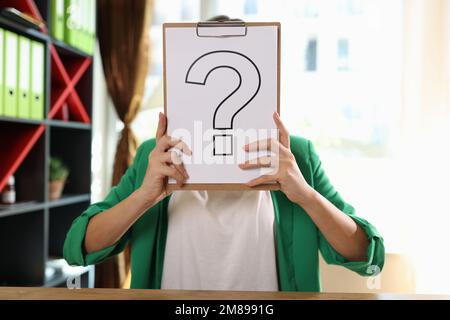 Business woman holding question mark in front of her face in office. Stock Photo