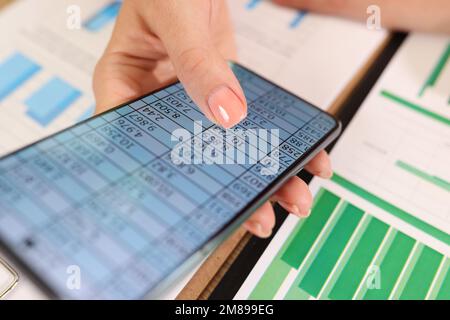 Close up of business woman hand with financial data on smartphone screen and office table with documents. Stock Photo