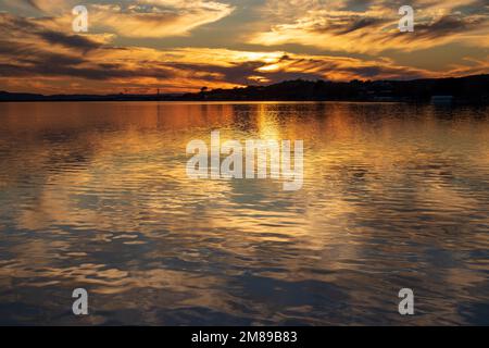 Sunset over Inks Lake at Inks Lake State Park Texas USA. The sky glows as the reflections of the clouds glimmer with the golden light casting shadows. Stock Photo