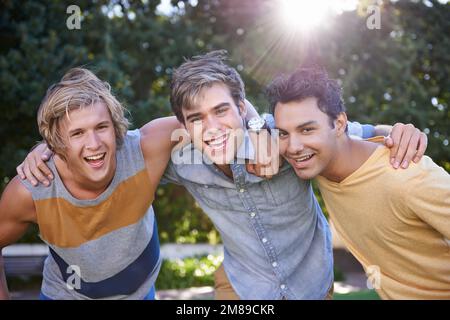 We get by with a little help from our friends. Portrait of three smiling friends standing with arms around each other in a park. Stock Photo
