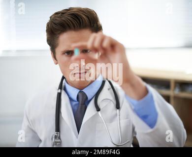 Small dose equals a big cure. a young doctor looking at pill he is holding. Stock Photo