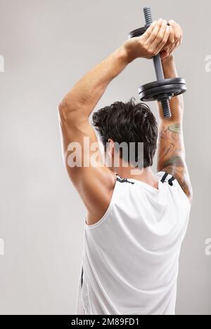 Working those biceps. Rearview of a young man working on his triceps using dumbbells. Stock Photo