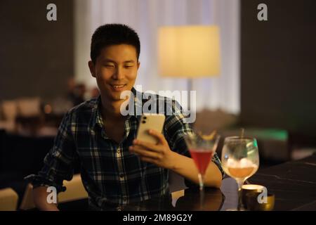 smiling Asian young man look at phone at night bar counter Stock Photo