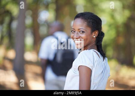 Letting him take the lead for a change...Portrait of a young african american woman hiking in the woods with her husband in the background. Stock Photo