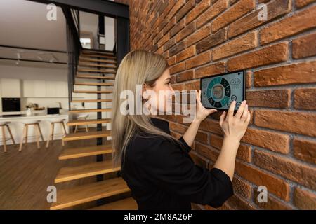 young woman using smart home app to control light turning on with tablet pc Stock Photo