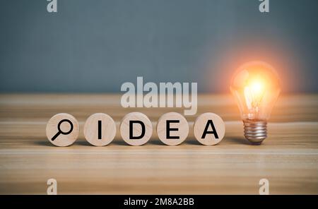 Idea text and find symbol on circular wooden block with shining lightbulb. Creative success idea inspiration business concept innovation solution On t Stock Photo