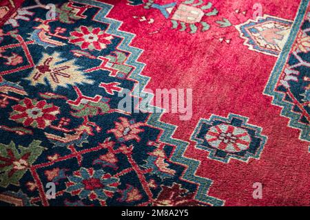 Oriental woolen carpet with traditional colorful ornaments over red background. Close up photo Stock Photo