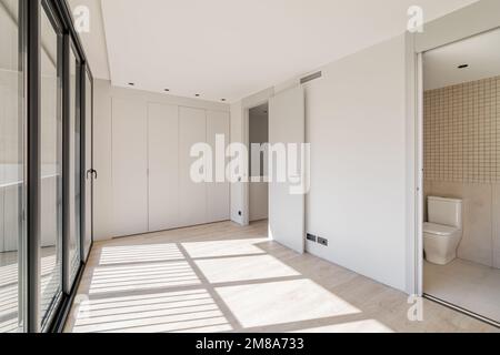 An empty room with built-in wardrobe in entire wall. With separate rooms for toilet and laundry. Room with large windows throughout wall through which Stock Photo