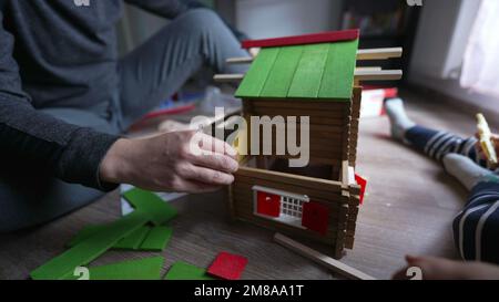 Child playing in room with mother building traditional wooden home toy. Little boy builds house with parent 2 Stock Photo