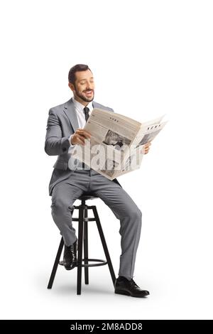 Young professional man in a suit sitting and reading a newspaper isolated on white background Stock Photo
