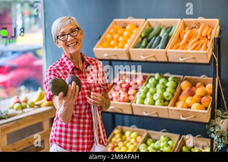 Woman is shopping in fruits and vegetables store. She is picking avocado. Stock Photo