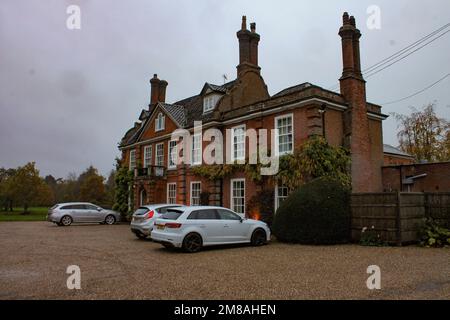 The two-story brick private house with windows with white bars and cars parking in the yard by the beautiful garden in London, UK Stock Photo