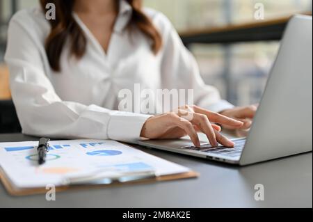cropped shot, Professional and focused millennial businesswoman or female accountant using laptop computer, working on her financial tasks. Stock Photo