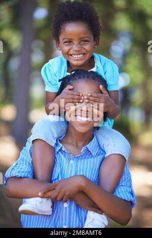 Sibling bonding in the great outdoors. Portrait of a little girl covering her brothers eyes while being carried on his shoulders. Stock Photo