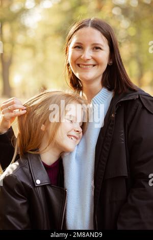 Portrait of stunning beautiful family of young woman and teenage girl standing, embracing in forest park in autumn. Stock Photo