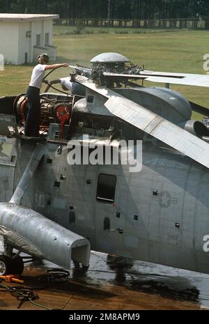 A maintenance crewman hoses off the folded-back rotor blades of a Helicopter Combat Support Squadron 16 (HC-16) SH-3D Sea King helicopter. Base: Naval Air Station, Pensacola State: Florida (FL) Country: United States Of America (USA) Stock Photo