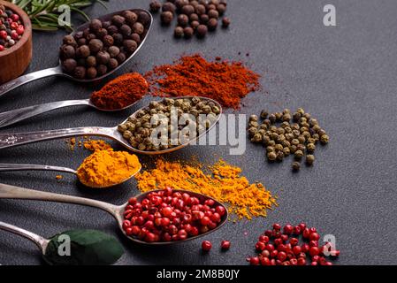 Several types of spices in metal spoons paprika, tomatoes, curry, beets, cumin, turmeric, fennel, spirulina, allspice of different colors on a black c Stock Photo